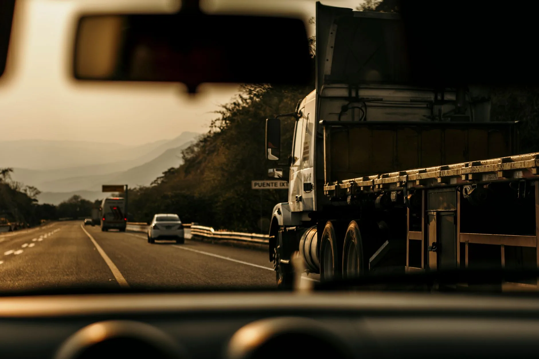 Tractocamión con plataforma circula por una autopista de Chiapas al atardecer, visto desde otro vehículo