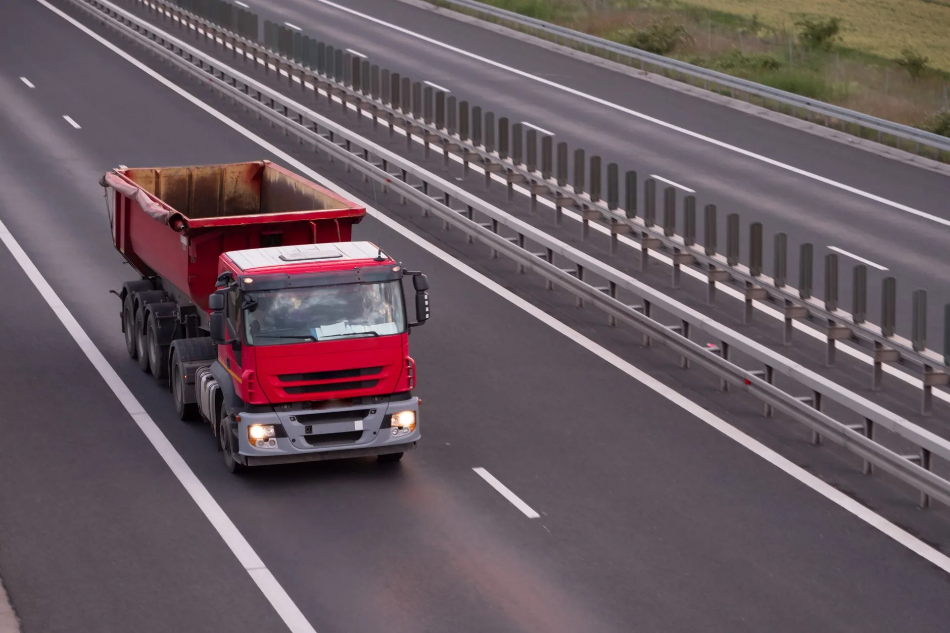 Camión de volteo rojo circulando por una autopista de varios carriles con barrera metálica