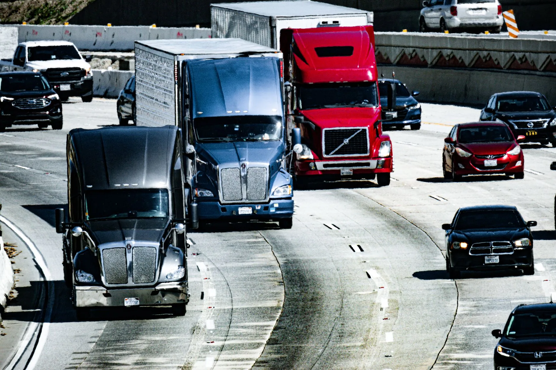 Tractocamiones con caja seca y autos avanzan por una autopista de varios carriles con tráfico denso